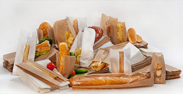 Assortment of eco-friendly paper food packaging, including sandwich bags, baguette sleeves, and bakery wrappers, displayed with fresh food items