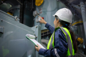 Engineer inspects equipment with clipboard in industrial facility wearing safety helmet and reflective vest showing focus and professionalism